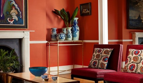 Deep orange walls with red chairs and patterned cushion in lounge